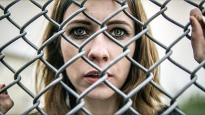 Huvudpersonen Linda i närbild bakom hönsnät på fängelsets gård i isländska tv-serien Fångar