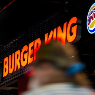 Nuori kävelee Burger King mainoskyltin alta.