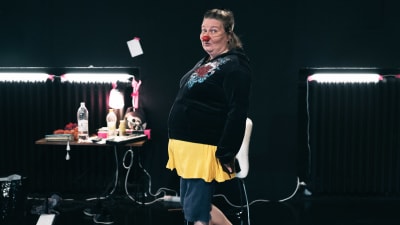 En kvinna med clownnäsa tittar in i kameran.  
