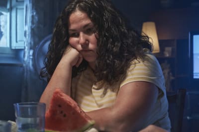 Närbild på en ledsen Sara (Laura Galán) som sitter vid köksbordet.