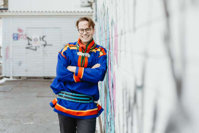 Janne Hirvasvuopio i  sameklädsel, lutar sig mot en graffitivägg.  