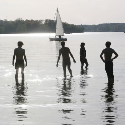Ungdomar i vattnet och en segelbåt.