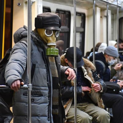 Människor på metron i Moskva. En man bär en gasmask, de andra munskydd.