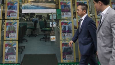 Två män framför en fastighetsförmedling i Hongkong.