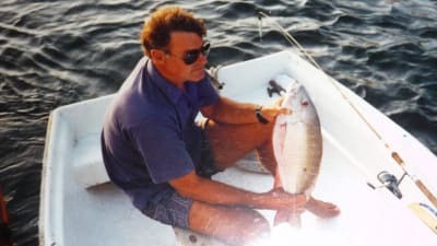 Bild på Seppo Sarekoski i en glasfiberbåt. Han har fått napp, en stor fisk i famnen.