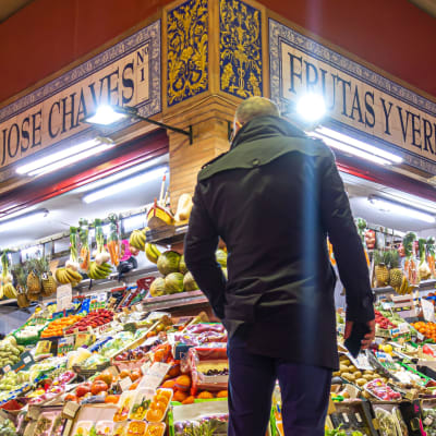 En man står framför en färgglad och ljus frukthandel. Sevilla, södra Spanien.