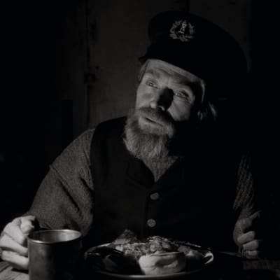 Thomas (Willem Dafoe) sitter vid bordet och äter.