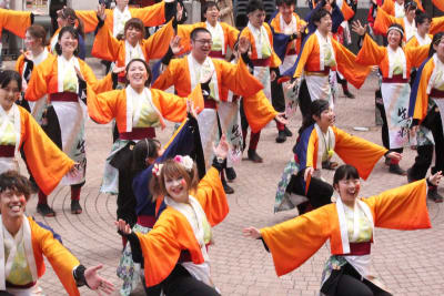 En grupp dansare som utför den japanska dansen yosakoi. De bär alla dräkter i orange. Dräkterna har vida ärmar.