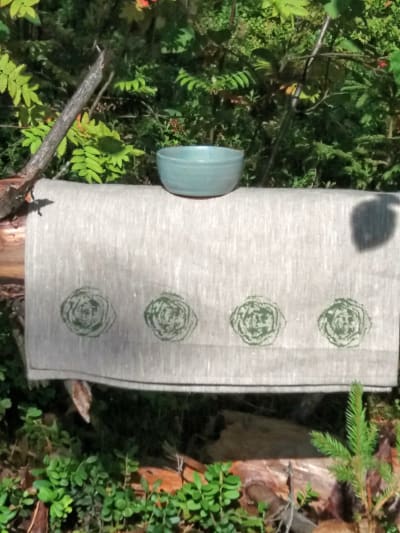 En linneduk och en skål ute på en bänk i naturen.
