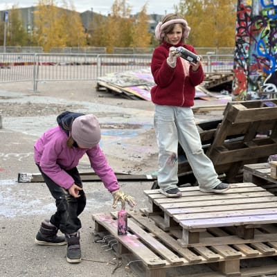 Två flickor står vid Söderviks skejt- och graffitipark och målar.