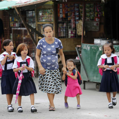 En filippinsk mamma tar sina barn till skolan i huvudstaden Manila.