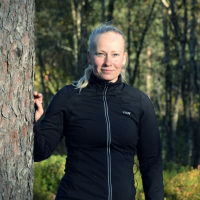 En kvinna lutar sin hand mot ett träd och lér mot kameran.