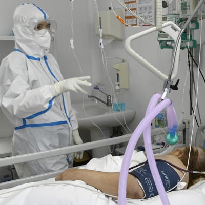 En sjukskötare i skyddsutrustning står vid en sjukhussäng där en coronapatient ligger.