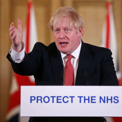 Storbritanniens premiärminister Boris Johnson talar vid ett talarpodium 22.3.2020. Han har sträckt ut högra handen.