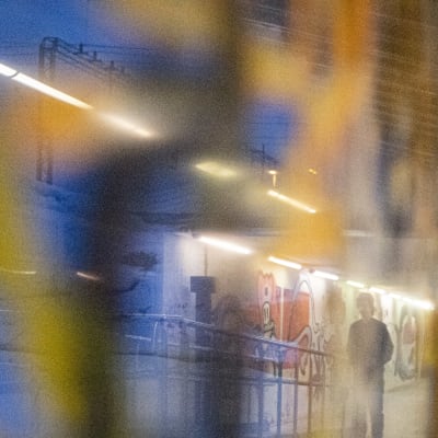 Poika kävelee hämärässä käytävässä. Kuvassa näkyy epäselviä värejä ja graffiteja. 