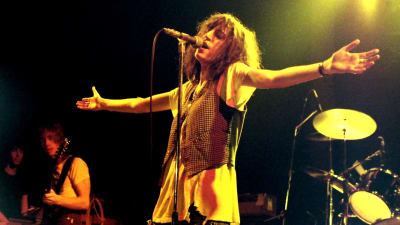 Patti Smith uppträder år 1978. Hon sjunger vid mikrofonen med armarna usträckta åt sidorna.
