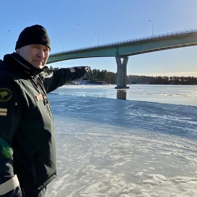 En sjöbevakare står och pekar ut mot isen under Emsalö bro.