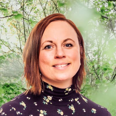 Anna Bertills småler in i kameran framför en grönskande bakgrund.