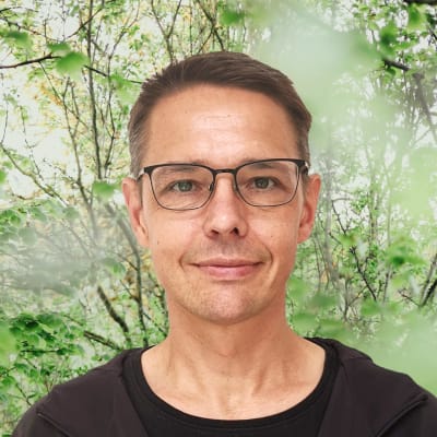 Olof Schybergson småler in i kameran. Bakgrunden är en grönskande skogsdunge.