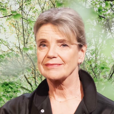 Stina Ekblad småler in i kameran. Bakgrunden är en grön skogsdunge.