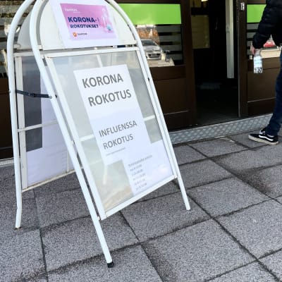 Korona- ja influenssarokotuksista kertova kyltti Hatanpään koronarokotusyksikön ovilla.