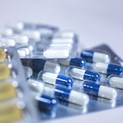 Olika mediciner i sina plastförpackningar i närbild. I fokus medicintabletter som är har ett hölje i blått och vitt.