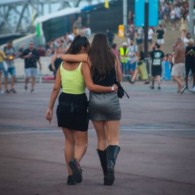Kaksi minihameeseen pukeutunutta naista kävelee halaillen festivaaliyleisön keskellä. 