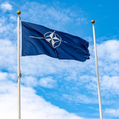 Militäralliansen Natos flagga avtecknar sig mot en ljusblå och delvis molnig himmel.