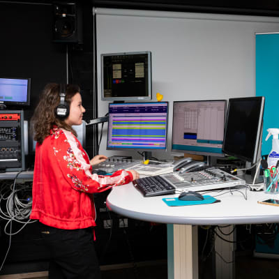 Nainen ja mies seisovat vastakkain eri puolilla radion lähetyspöytää ja katsovat toisiaan.