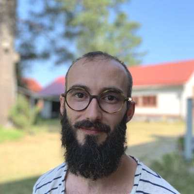 Mansperson står utomhus i sommargrönska.