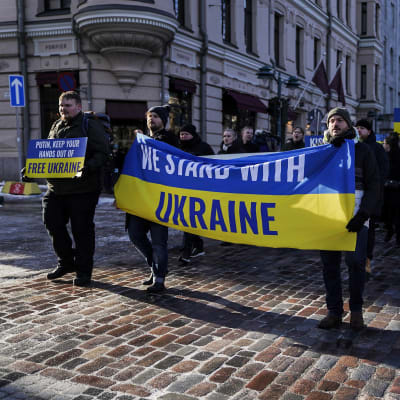 Demonstrationer håller i plakat och flaggor med texten "We stand with Ukraine" i Helsingfors den 26 februari 2022.