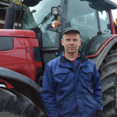 En man, bonde, står framför sin traktor.