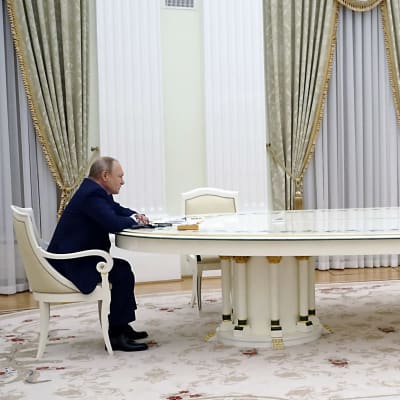 Rysslands president Vladimir Putin sitter vid ett vitt förhandlingsbord mittemot Frankrikes president Emmanuel Macron. 