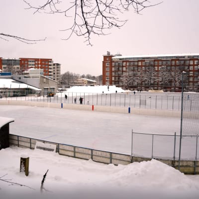 Ishockeyrink och skridskobana i en stad med höghus i bakgrunden.