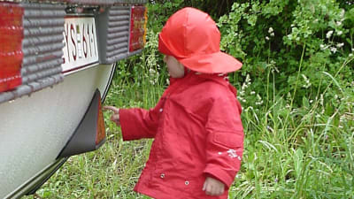 ett litet barn i röda regnkläder rör i bakändan av en bil.