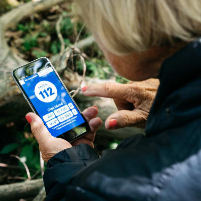 Kuvassa vanhus on metsässä ja avaa kännykästä 112-sovelluksen
