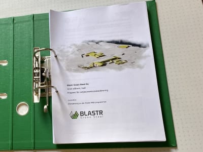 En grön mapp med papper där där det står Blastr och som visar bilder på ett planerat fossilfritt stålverk i Ingå.