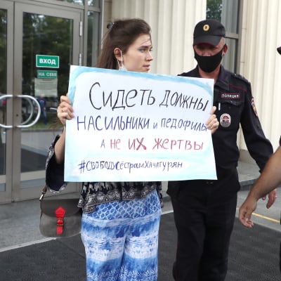 En demonstrant håller upp ett plakat. Två vakter står bredvid henne