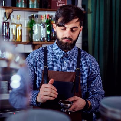 En person står bakom en bardisk i ett kafé och lagar kaffe.