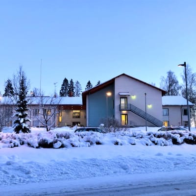 Ett tvåvåningshus i skymningstimmen, vinter, stort hus, det är ett äldreboende. Snö, gatulyktor.