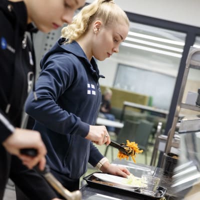 Linnea Ceder ja Sani Mäkelä ottamassa ruokaa Mäkelänrinteen urheilulukion ruokalassa.