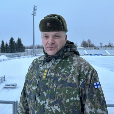 Kapteeni Juho Kangas seisoo talvisen stadionin edustalla armeijan maastepuvussa. 