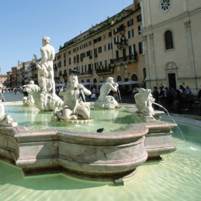 Suihkulähde, jossa useita vettäsylkeviä patsaita, Piazza Navonalla Roomassa. Talot ympäröivät aukiota.
