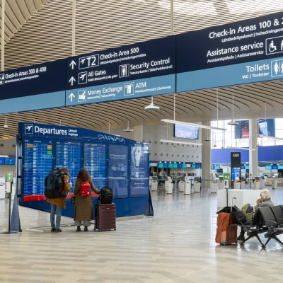 Helsinki-Vantaan lentoasema, uusi terminaali, matkustajia lentävien lähtöjen taulun edessä.