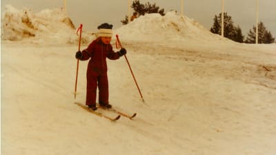 Gulnat foto av liten Tanja Poutianen som skidar i en brun halare. 