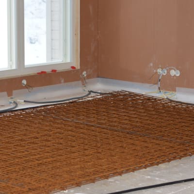 rostigt armeringsjärnnät på ett betonggolv inne i ett halvfärdigt nytt hus.