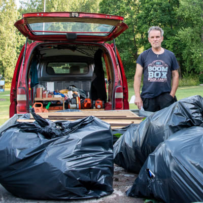En man står vid en röd paketbil med en släpvagn. I släpvagnen finns stora svarta plastsäckar.