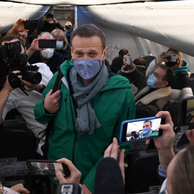 Aleksej Navalnyj ombord på ett flygplan 17 januari 2021. Han bär munskydd. Runt honom står massvis av människor som fotograferar honom.