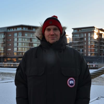 Porträtt av en man som poserar framför en frusen aura å. mannen är vinterklädd och bakom honom finns en tross mmed rimfrost över sig. 
