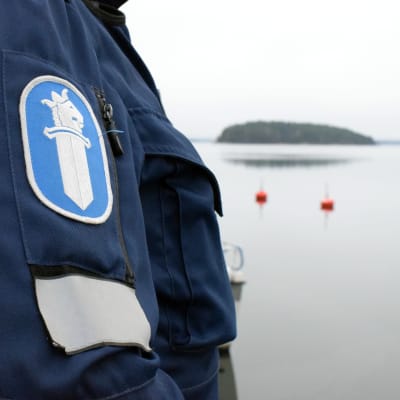 Polisens logotyp på ärmen av en polisrock. Havet och två röda bojar i bakgrunden.